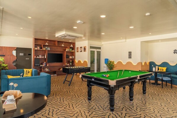 Eine Lounge mit Billardtisch, Sofas und einer Bücherwand.