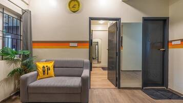 A hotel lobby with a sofa, a clock, a door, and a plant.