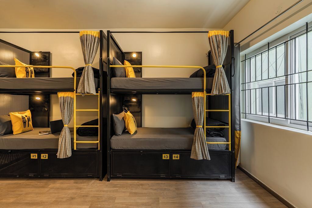 A dormitory room with bunk beds, each with a curtain, a bedside table, and a lamp.