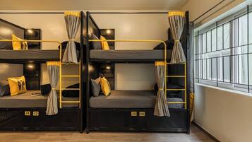 A dormitory room with bunk beds, each with a curtain, a bedside table, and a lamp.