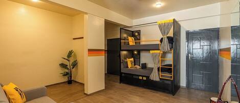 Una habitación con literas, un sofá, una planta en maceta y una guitarra.