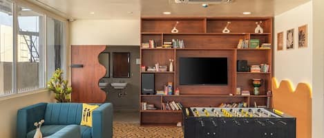 A modern living room with a sofa, a foosball table, a bookshelf, and a flat-screen TV.