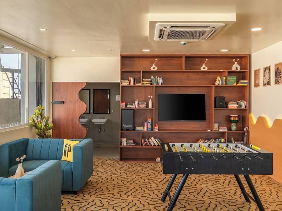 A modern living room with a sofa, a foosball table, a bookshelf, and a flat-screen TV.
