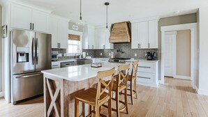 A modern kitchen with white cabinets, stainless steel appliances, and a large island with bar stools. - Afton Awaits (Afton)