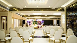 A hotel conference room with rows of white chairs, a stage with a floral backdrop, and a chandelier. - TOS Residency Jublee Hills By OTABoostup (Hyderabad)