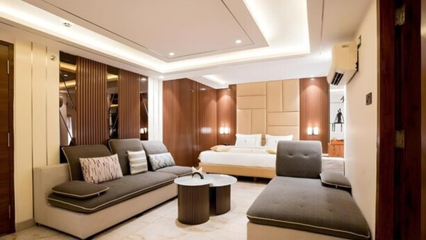 A modern living room with a sofa, armchair, and coffee table, a bed with headboard, and a wooden accent wall. - TOS Residency Jublee Hills By OTABoostup (Hyderabad)