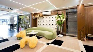 A modern lobby with a green sofa, a yellow plush toy, a potted plant, and a wall-mounted air conditioner. - TOS Residency Jublee Hills By OTABoostup (Hyderabad)