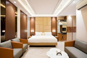 A modern hotel room with a large bed, two sofas, a coffee table, and a minibar.