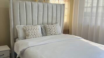 A bedroom with a large bed, a nightstand, a framed picture on the wall, and sheer curtains.