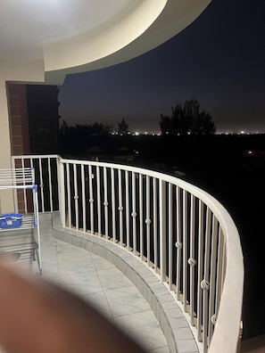 Ein Balkon mit weißer Brüstung, einem blauen Korb und einem gefliesten Boden.