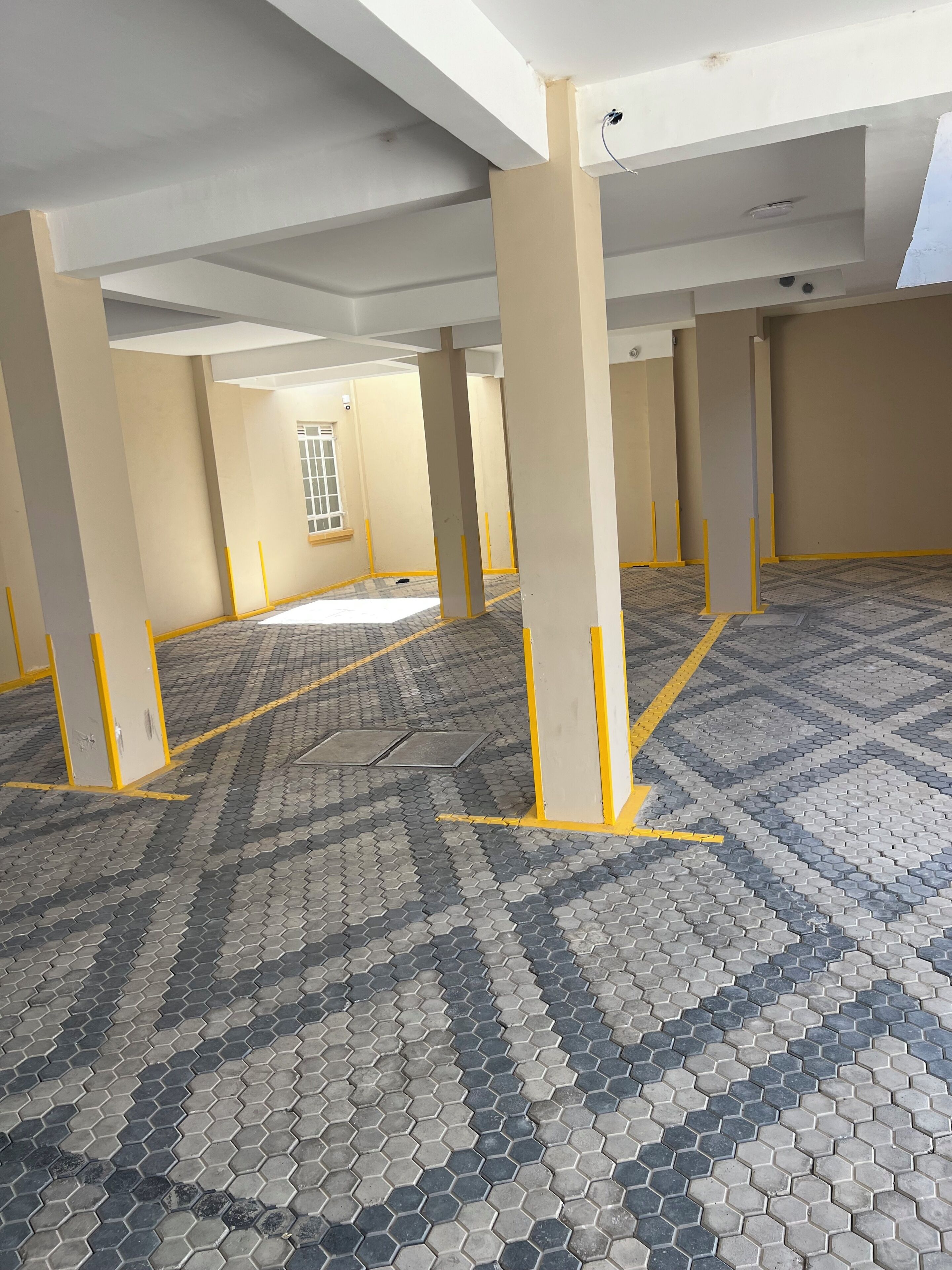 A spacious indoor area with tiled flooring, yellow-painted columns, and a window with a grid pattern.