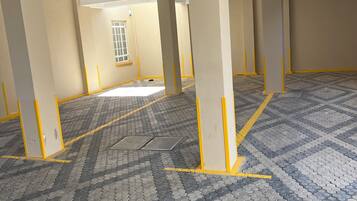 A spacious indoor area with tiled flooring, yellow-painted columns, and a window with a grid pattern.