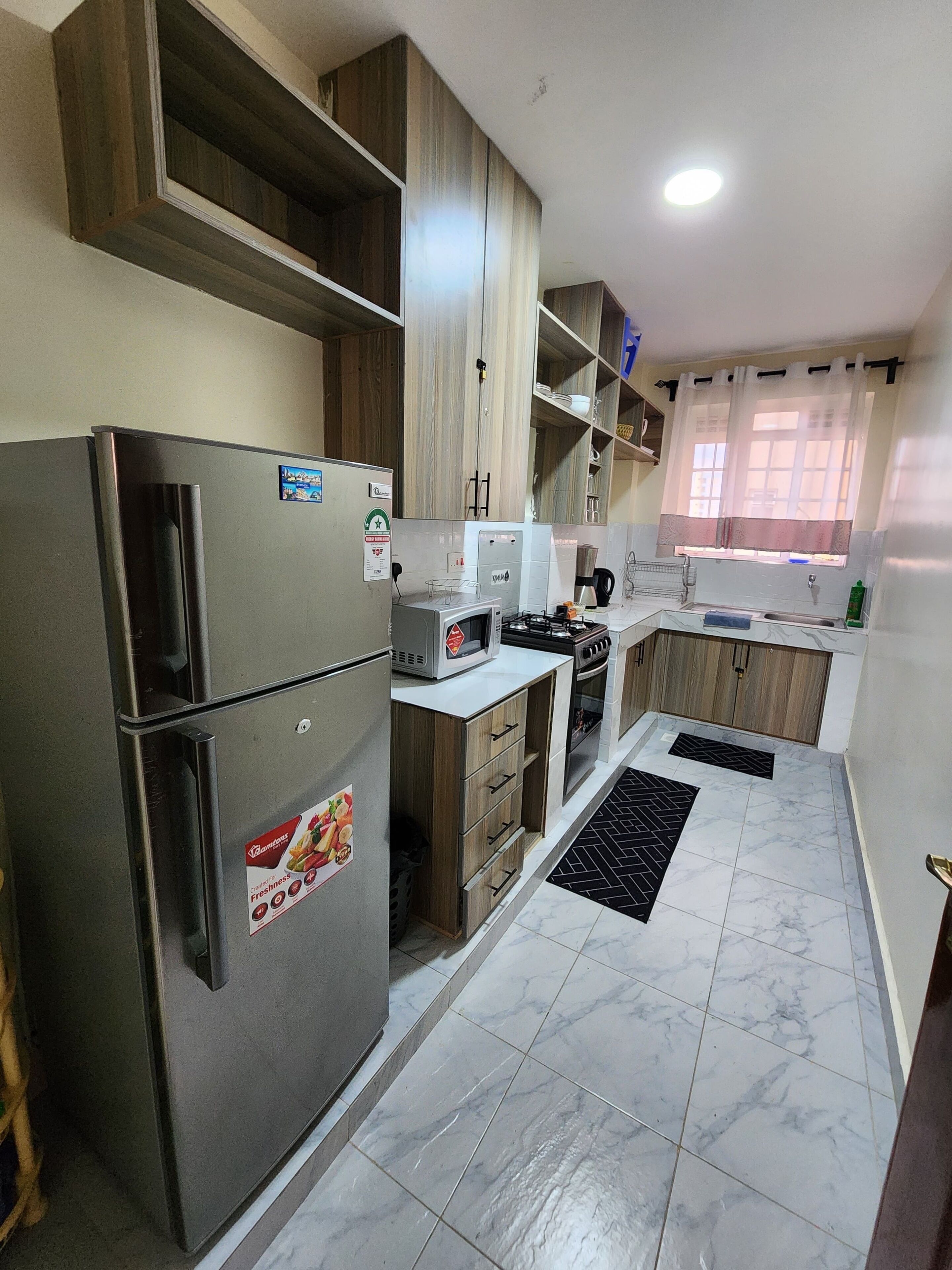 A modern kitchen with a refrigerator, microwave, stove, and wooden cabinets.