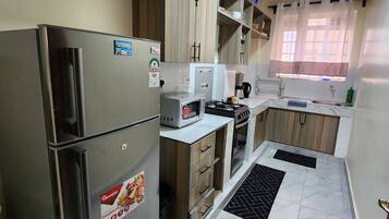 A modern kitchen with a refrigerator, microwave, stove, and wooden cabinets.