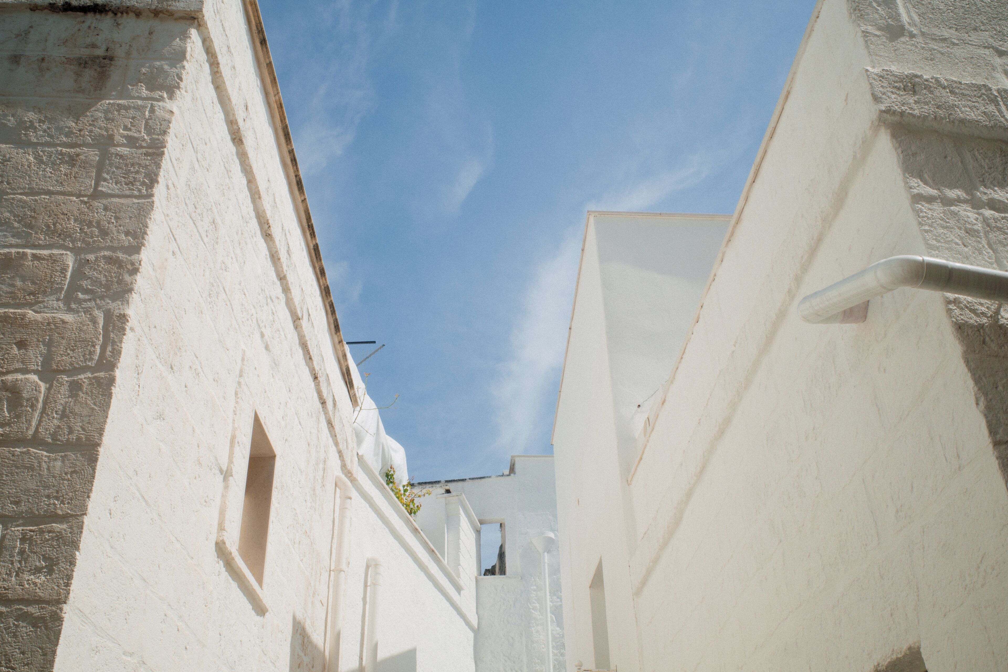 A narrow street with white buildings, a clear blue sky, and a visible window.
