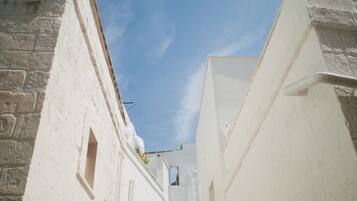 A narrow street with white buildings, a clear blue sky, and a visible window.