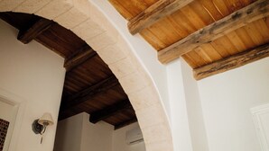An arched stone doorway leading to a room with a wooden ceiling and a white door. - Dimora Rossella (Monopoli)