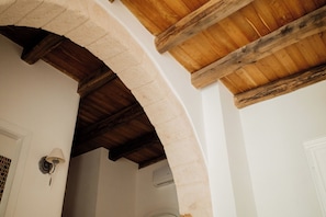 Un portail en arc surmontĂ© dâune arche en pierre, avec des poutres en bois, une porte blanche et un luminaire fixĂ© au mur.