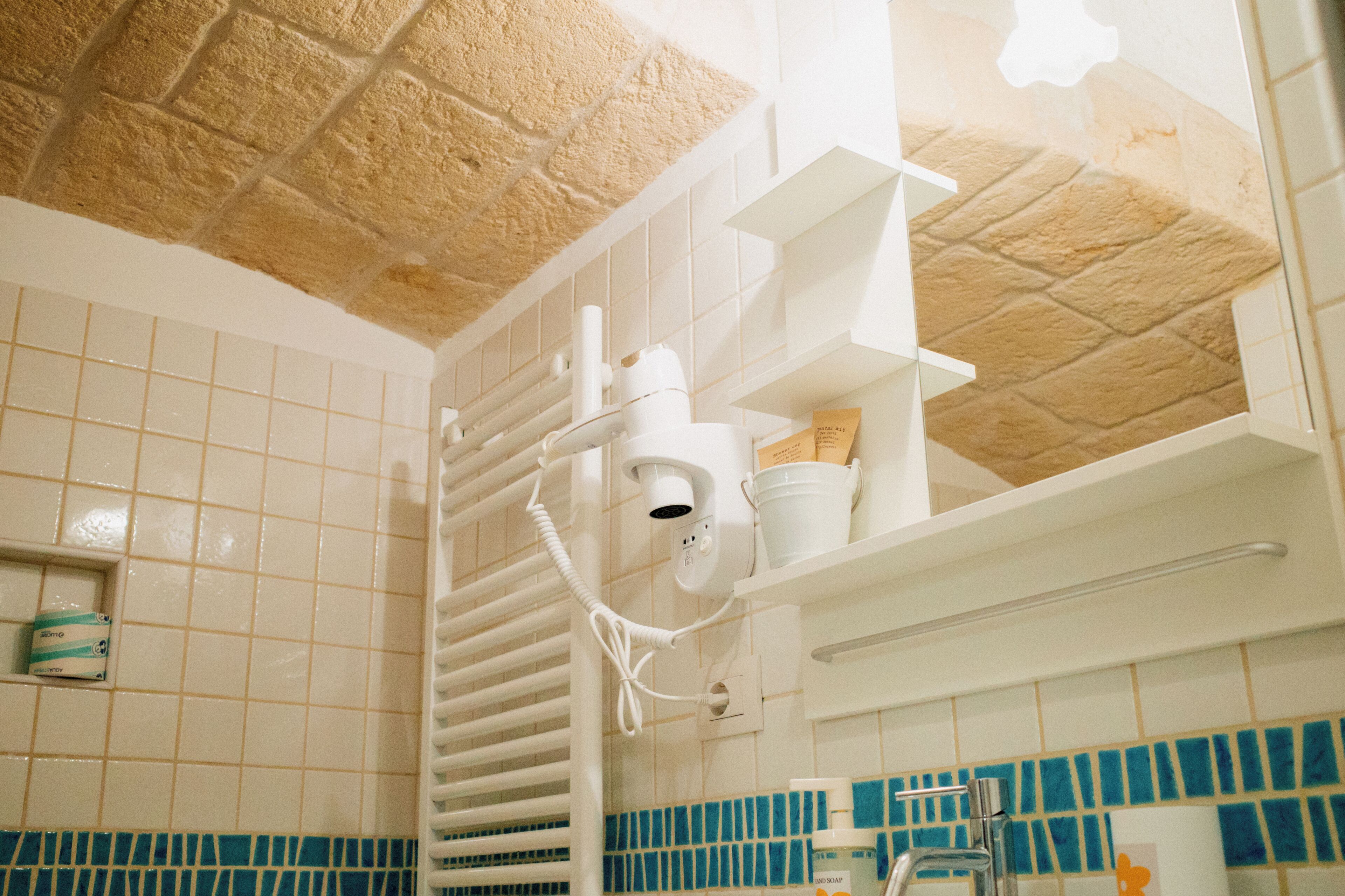 A bathroom with white tiled walls, a blue-tiled accent wall, a shower area, and a white ceiling with a textured pattern.