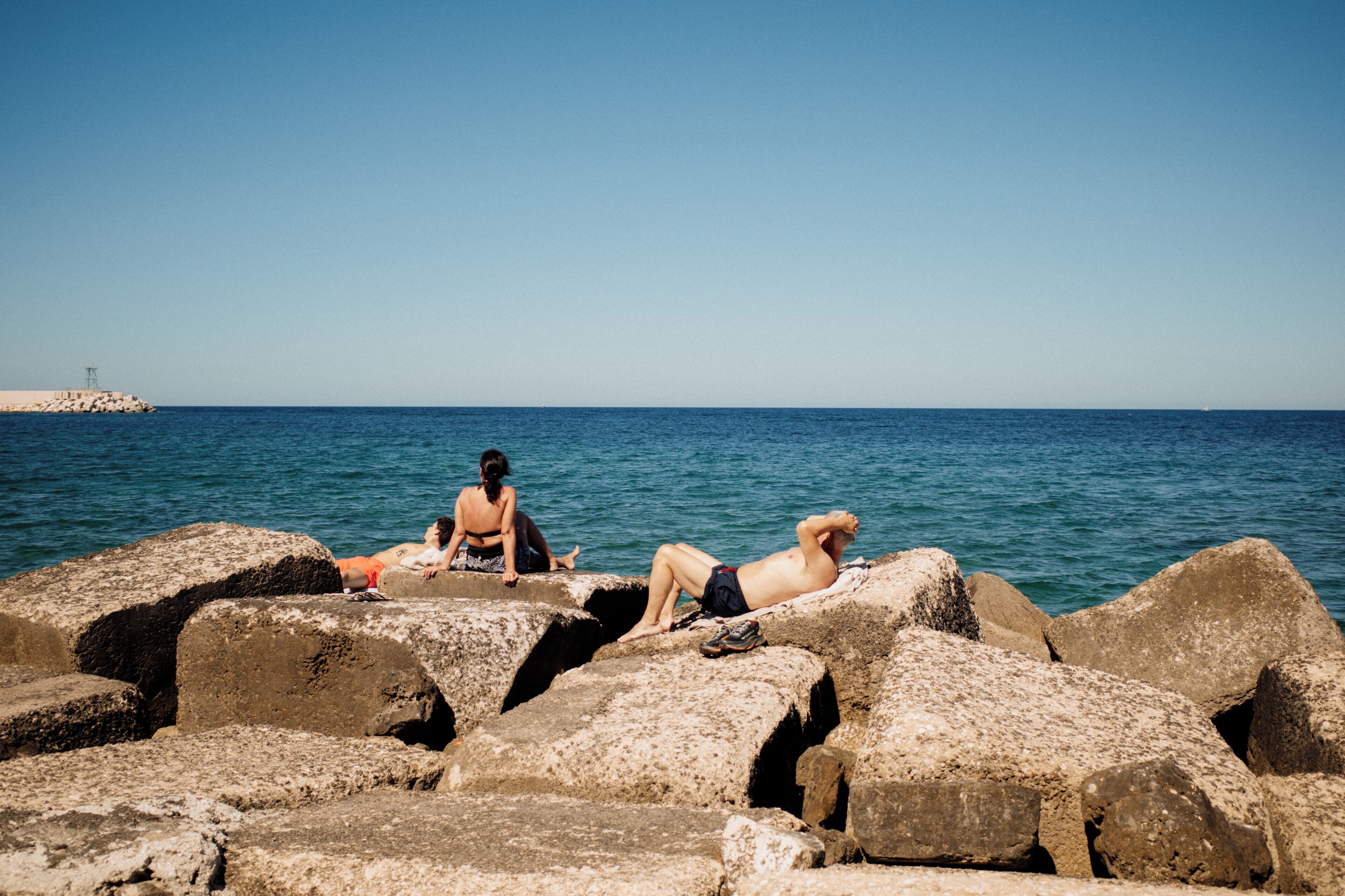 Una costa rocosa con dos personas descansando sobre las rocas.