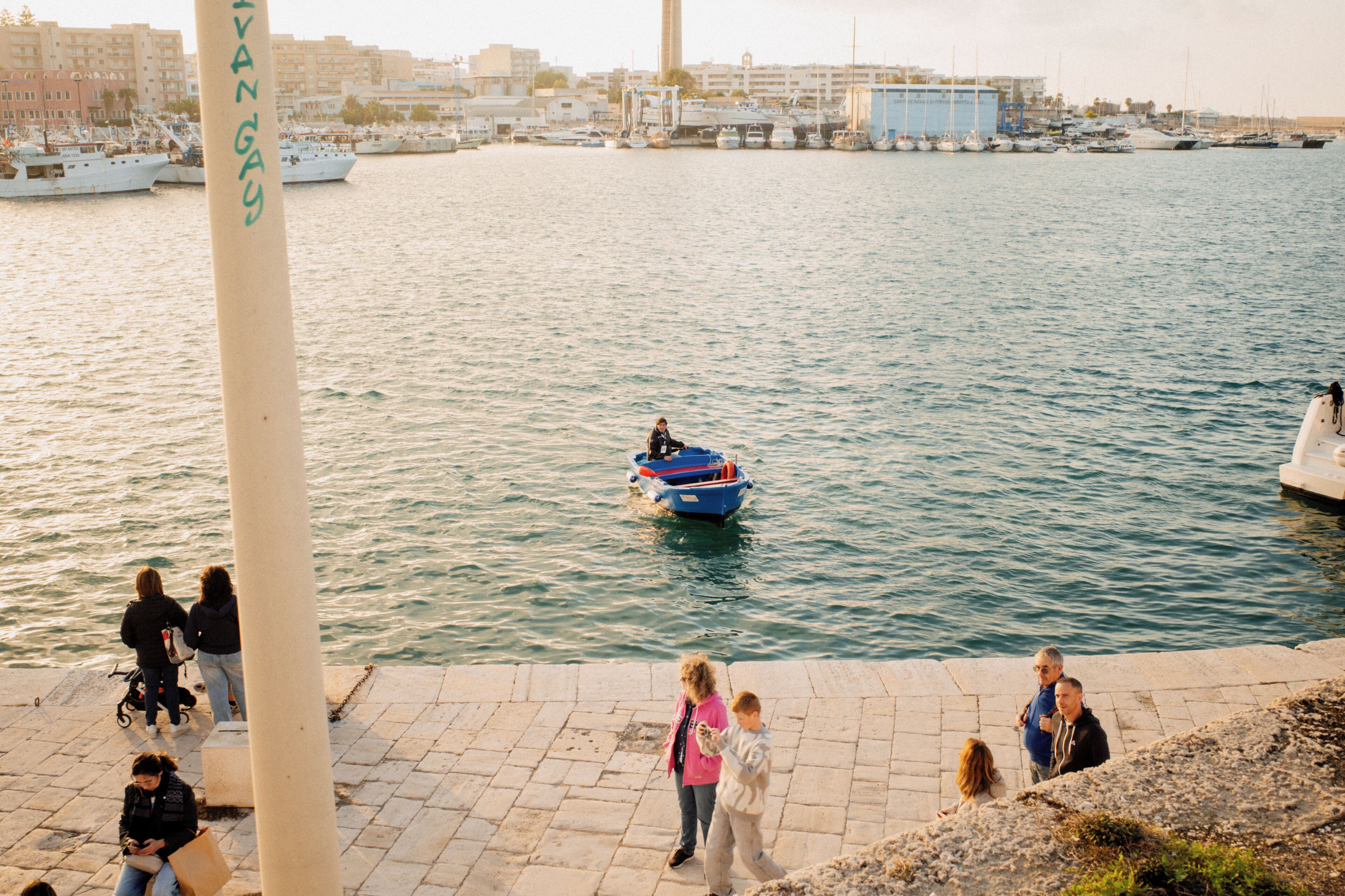 A waterfront area with boats, people walking, and a large white column.