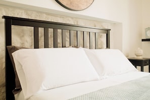 A bed with a wooden headboard, white bedding, and a small bedside table with a decorative item.