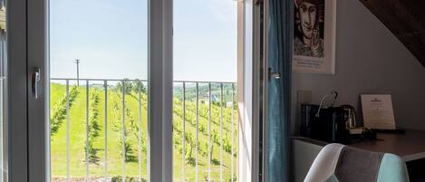 A room with a large window overlooking a vineyard, a chair, and a coffee machine on a table.