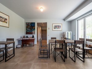 Ein Essbereich mit einem zentralen Tisch und Stühlen, ein Küchenbereich mit Herd und Schränken sowie Kunstwerke an den Wänden.