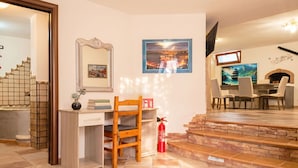 Een hotelkamer met een bureau, stoel, brandblusser, televisie en open haard.