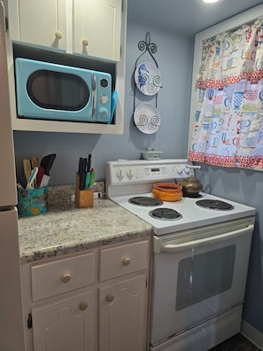 Una cocina con una estufa blanca, un microondas azul y un plato decorativo en la pared.