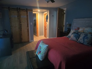 Un dormitorio con cama, escritorio, silla, ventilador de techo y puerta con un cartel.