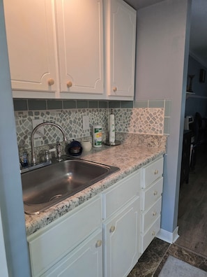 Una cocina con gabinetes blancos, encimera de granito y pileta de acero inoxidable.