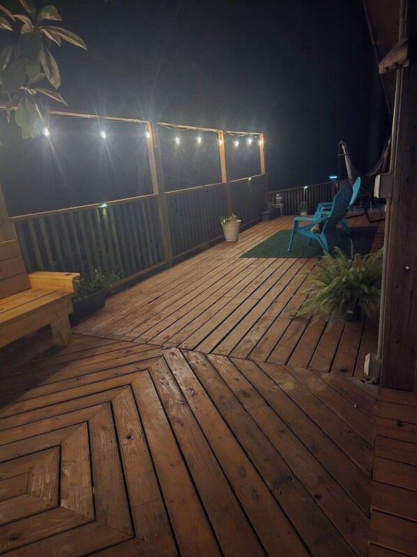 Una terraza de madera con luces colgantes, un banco y una silla.