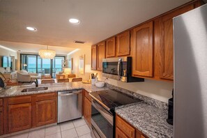 A kitchen with wooden cabinets, granite countertops, a stainless steel refrigerator, and a built-in microwave. - Beachfront 2B/2B Vacation Condo at Shamron Beach! Pool! Book Now For Dream Vacation! (Fort Myers Beach)