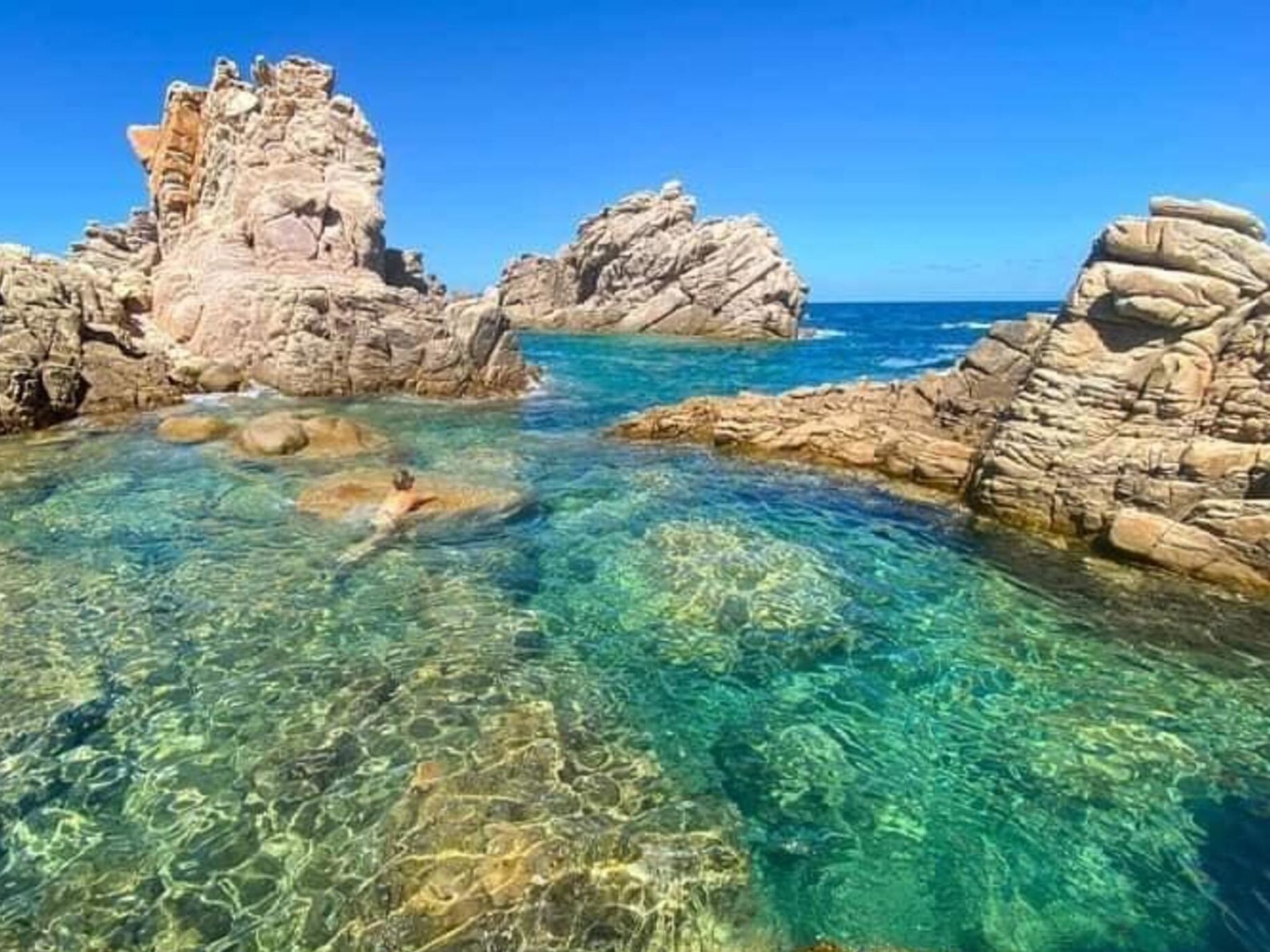 A coastal landscape with clear water, rocky formations, and a swimmer.