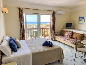 Ein Hotelzimmer mit Bett, einer Couch, einem Fernseher und einem Balkon mit Meerblick.