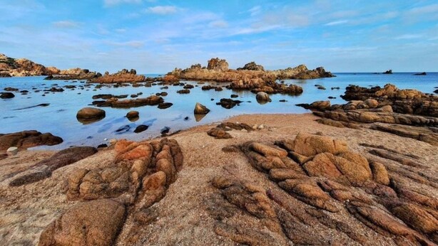 A rocky beach with clear water and a distant rocky formation. - Lavanda 2301 Bis by Interhome (Isola Rossa)