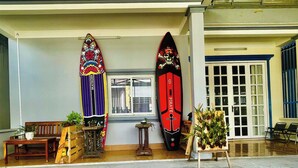 Two surfboards, a wooden bench, and a small table with plants in a room with a tiled floor and a window. - LŨA XÓM CHÀI là một homestay nằm ở làng chài Trần Phú, Dương Đông, Phú Quốc (Đặc khu Phú Quốc)