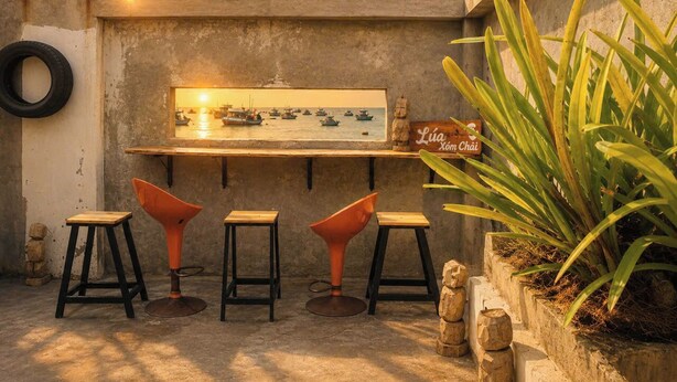 A bar area with stools, a sign reading 'Lúa Xom Chai,' and a view of boats on the water. - LŨA XÓM CHÀI là một homestay nằm ở làng chài Trần Phú, Dương Đông, Phú Quốc (Đặc khu Phú Quốc)