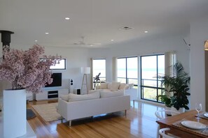 Ein modernes Wohnzimmer mit einem weißen Sofa, einem Flachbildfernseher, einem Teleskop und großen Fenstern mit Meerblick.