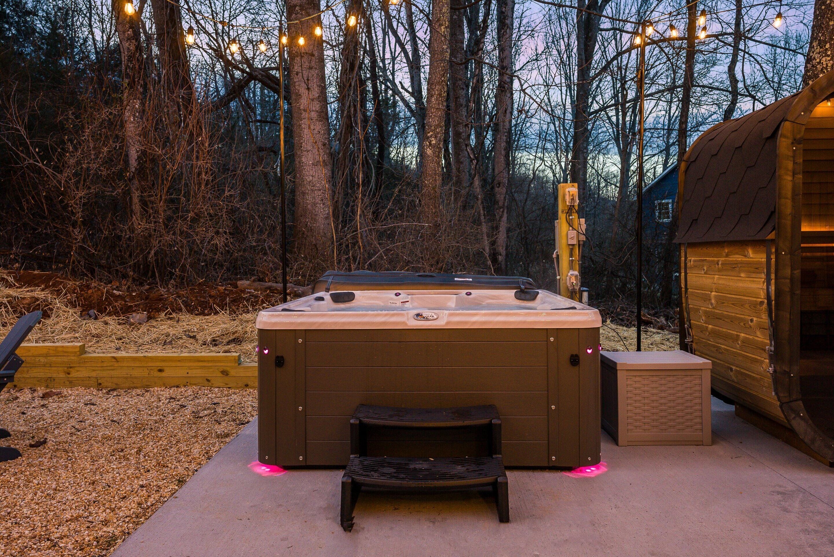 A hot tub with a wooden bench in a forested area with string lights.