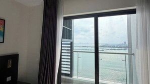 Una camera d'albergo con un'ampia porta scorrevole in vetro che dà su un balcone con vista su un corpo d'acqua e edifici in lontananza.