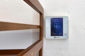 Un thermostat fixé au mur affiche une température de 18,3 °C, l’heure est 6 h 36 et le taux d’humidité est de 25 %.