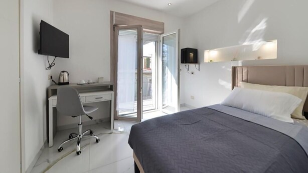 A modern hotel room with a bed, desk, chair, TV, and a sliding door to a balcony. - GIOIA E RELAX DI ZR  (Rho)