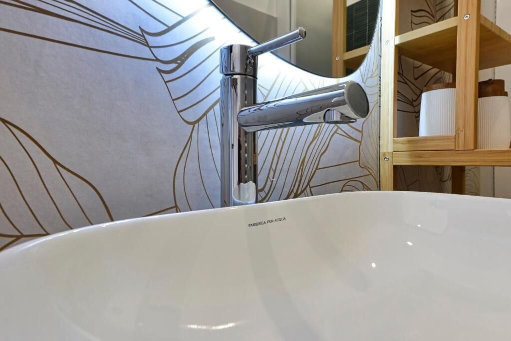 A bathroom with a white sink, chrome faucet, and a wooden shelf with toiletries.