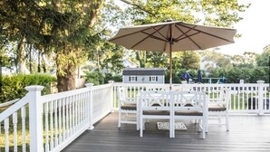 A wooden deck with white railings, a bench, and a table with an umbrella.
