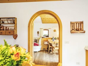 Una stanza con pavimento in legno, un divano bianco, un tavolo da pranzo con sedie e una zona cucina visibile attraverso un arco.