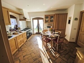 Uma cozinha com armários de madeira, uma mesa de jantar posta para quatro pessoas e vista para o exterior através de uma porta de vidro.