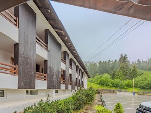 A building with a row of balconies, large columns, and a parking area with trees in the background. - Ciasina Alpina by Interhome (Folgarida)