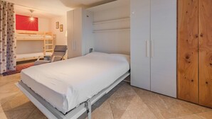 Ett sovrum med en enkelsäng, en våningssäng, en garderob och ett skrivbord med en stol.